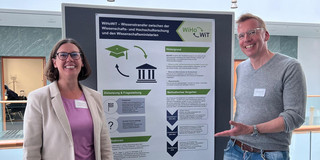 Two people in front of a display board with a poster.