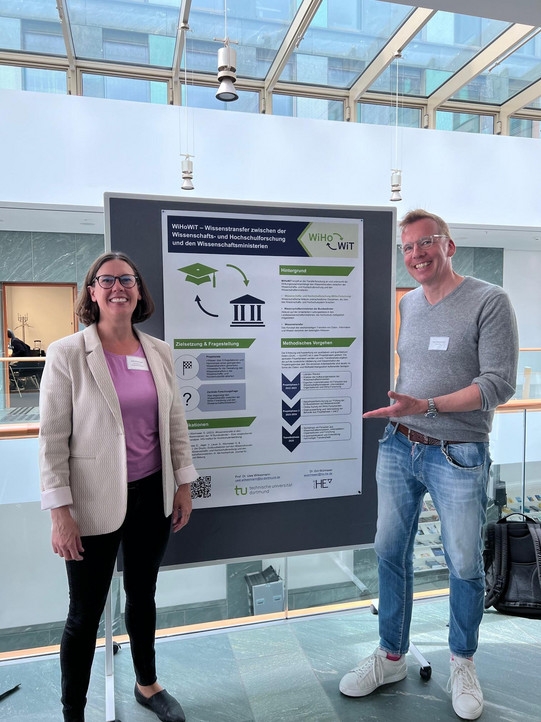 Two people in front of a display board with a poster.