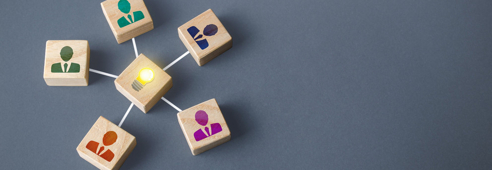Pictogram of people on 5 wooden cubes spread in a star shape around a pictogram of a light bulb on a wooden cube.